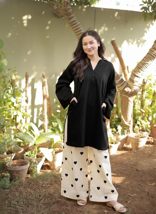Woman in black top and white pants with heart patterns standing in a garden.